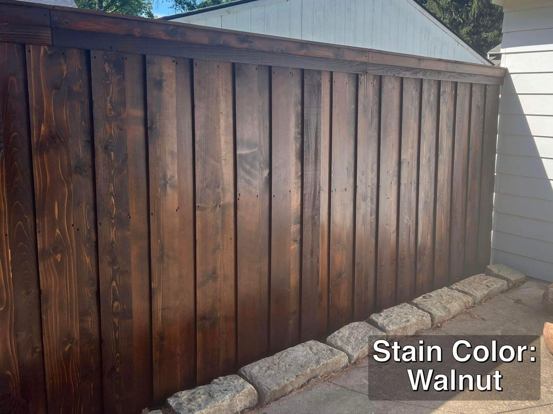 Wooden fence stained walnut, with stone border, in an outdoor setting.