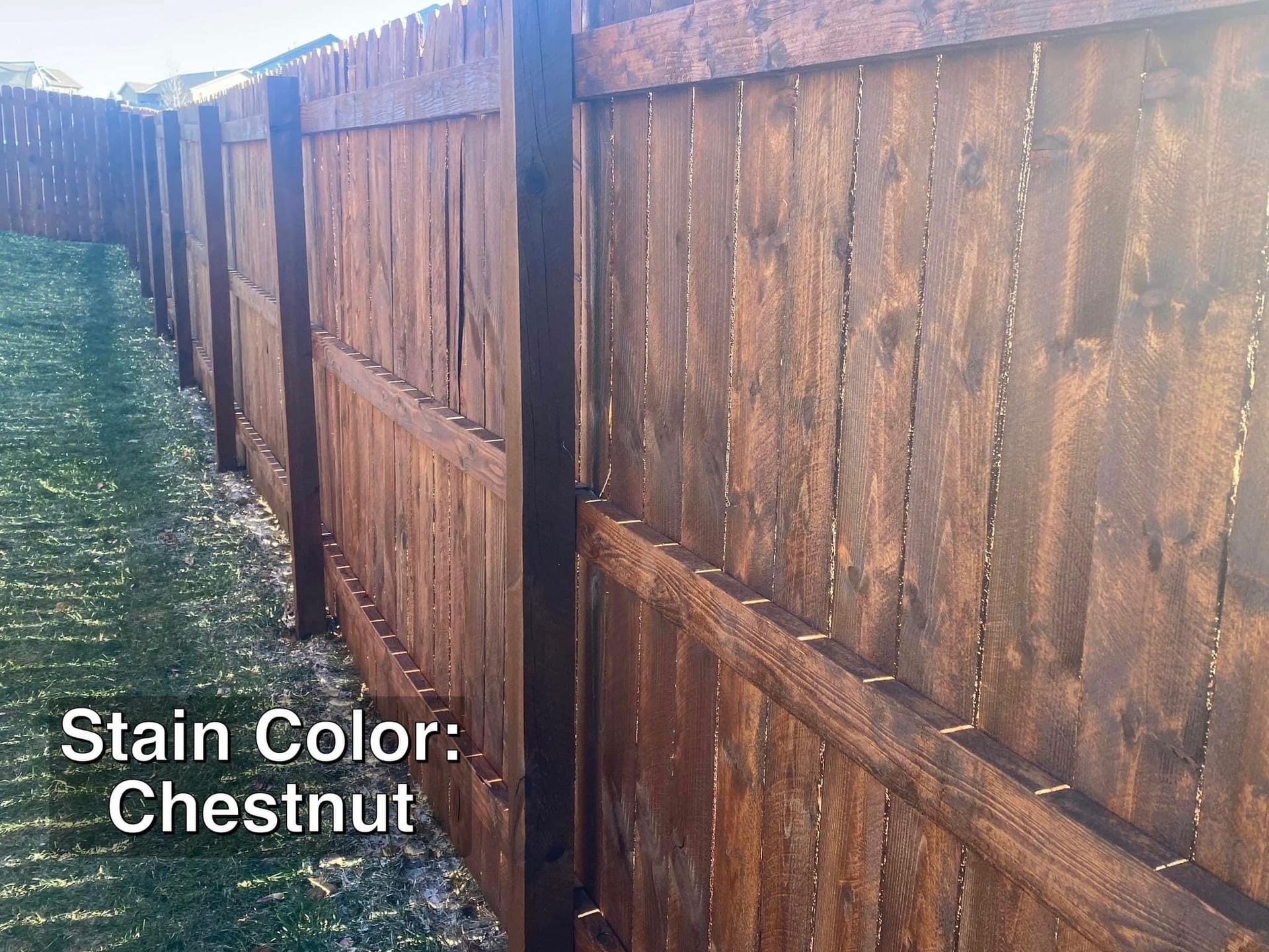Chestnut-stained wooden fence in a grassy outdoor setting. The fence is viewed at an angle, with a bright sky.