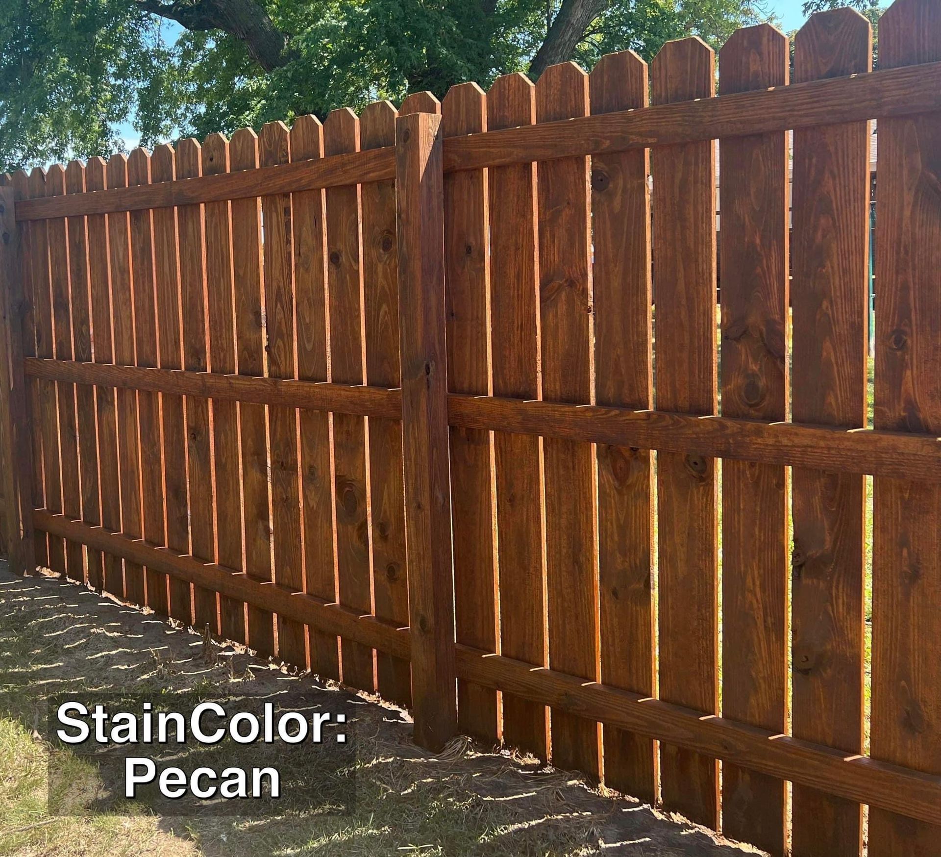 Brown pecan-stained wooden fence with pointed tops in a yard.