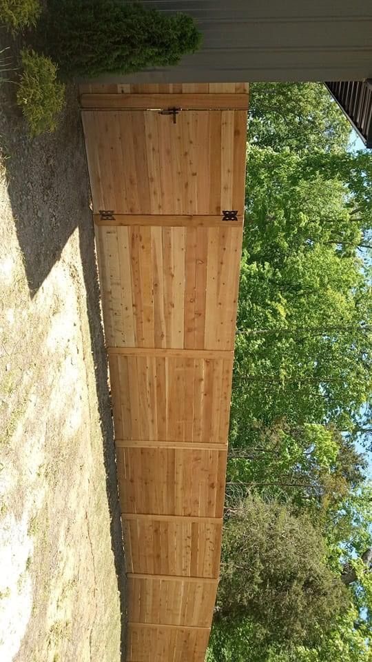 Wooden fence, vertical planks, with a gate and green trees in the background.