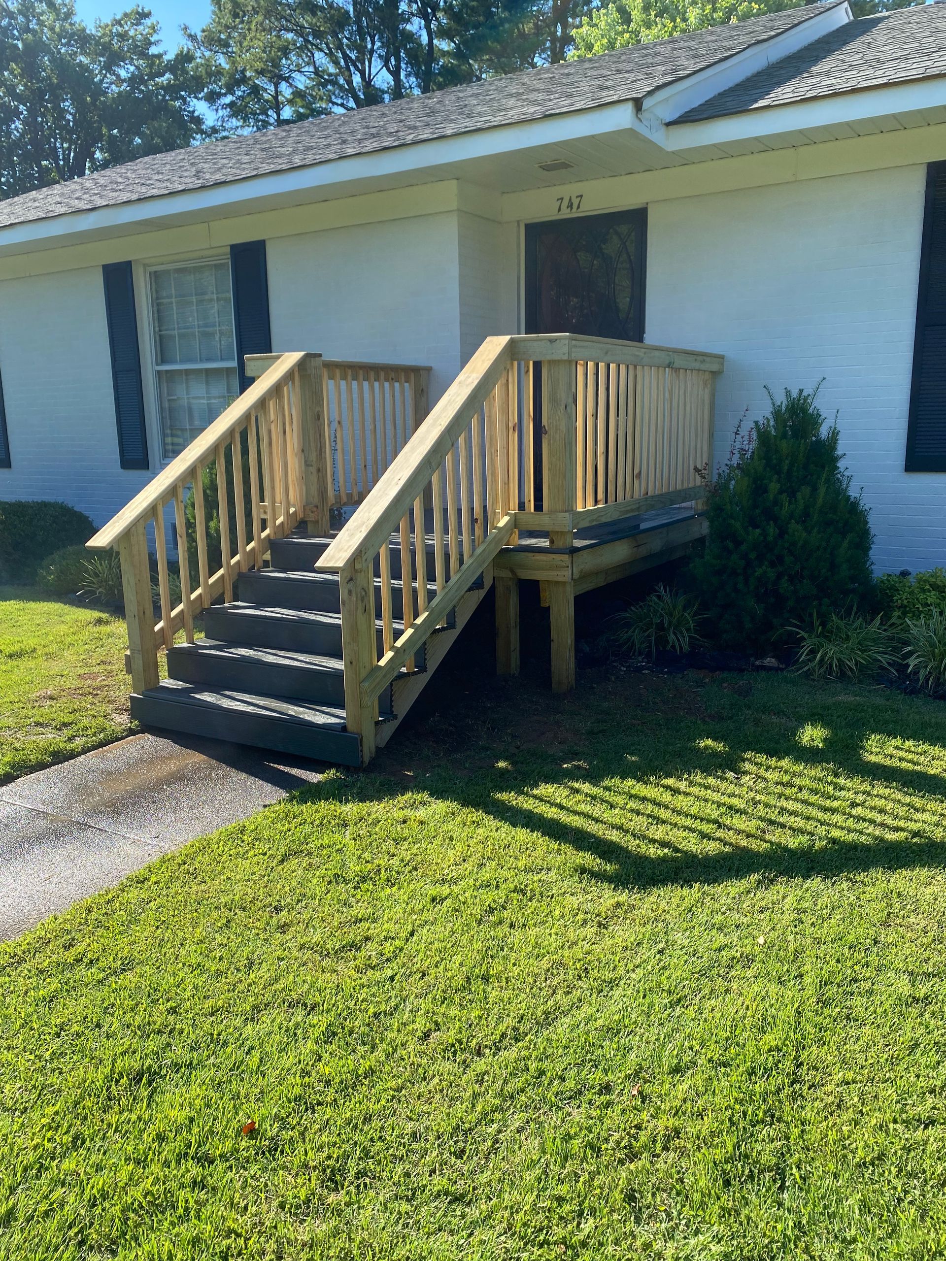 Wooden stairs and deck lead to a white building's entrance; green lawn surrounds.
