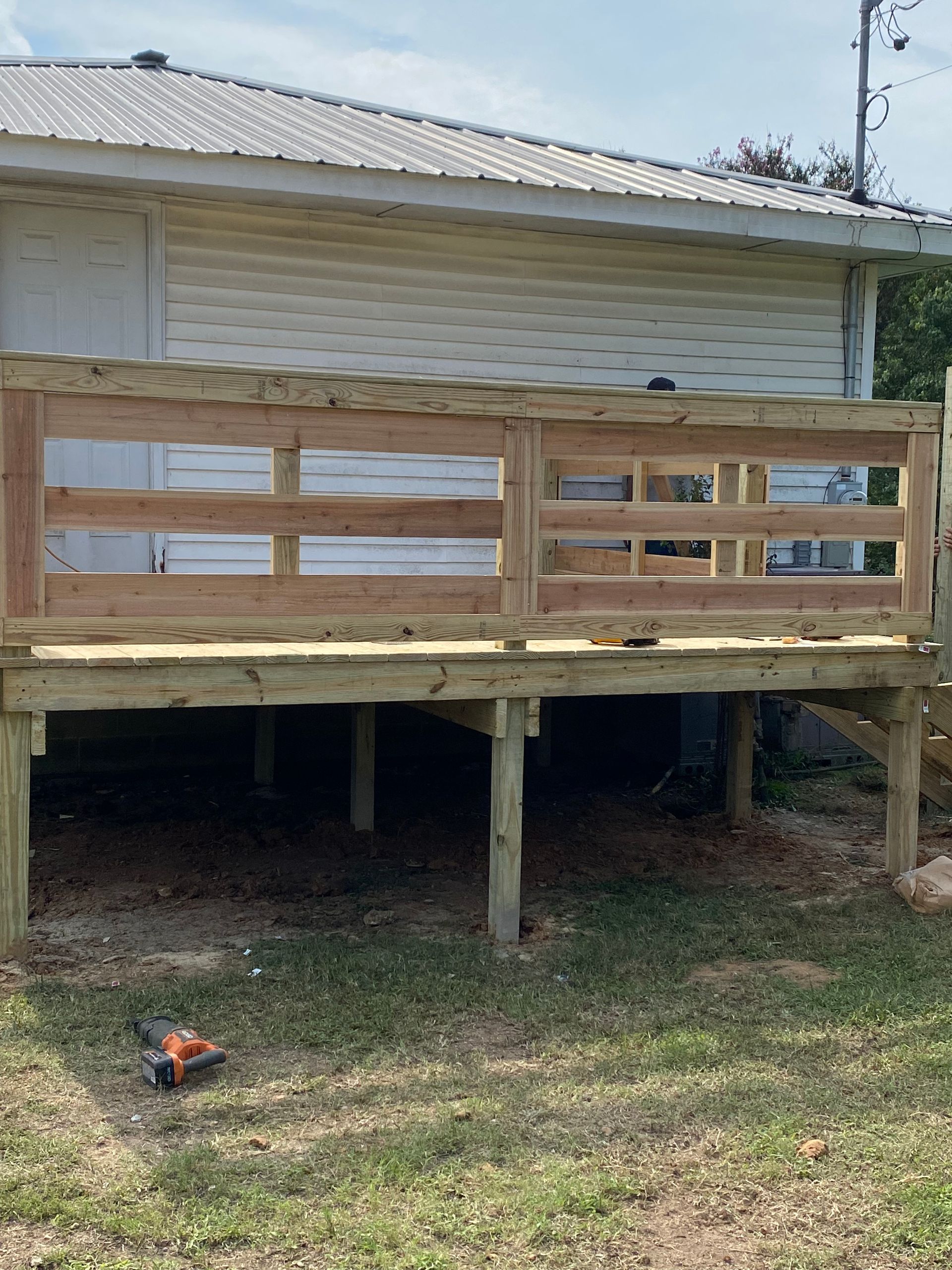 Wooden deck with railing, attached to a light-colored house, built in a grassy yard.
