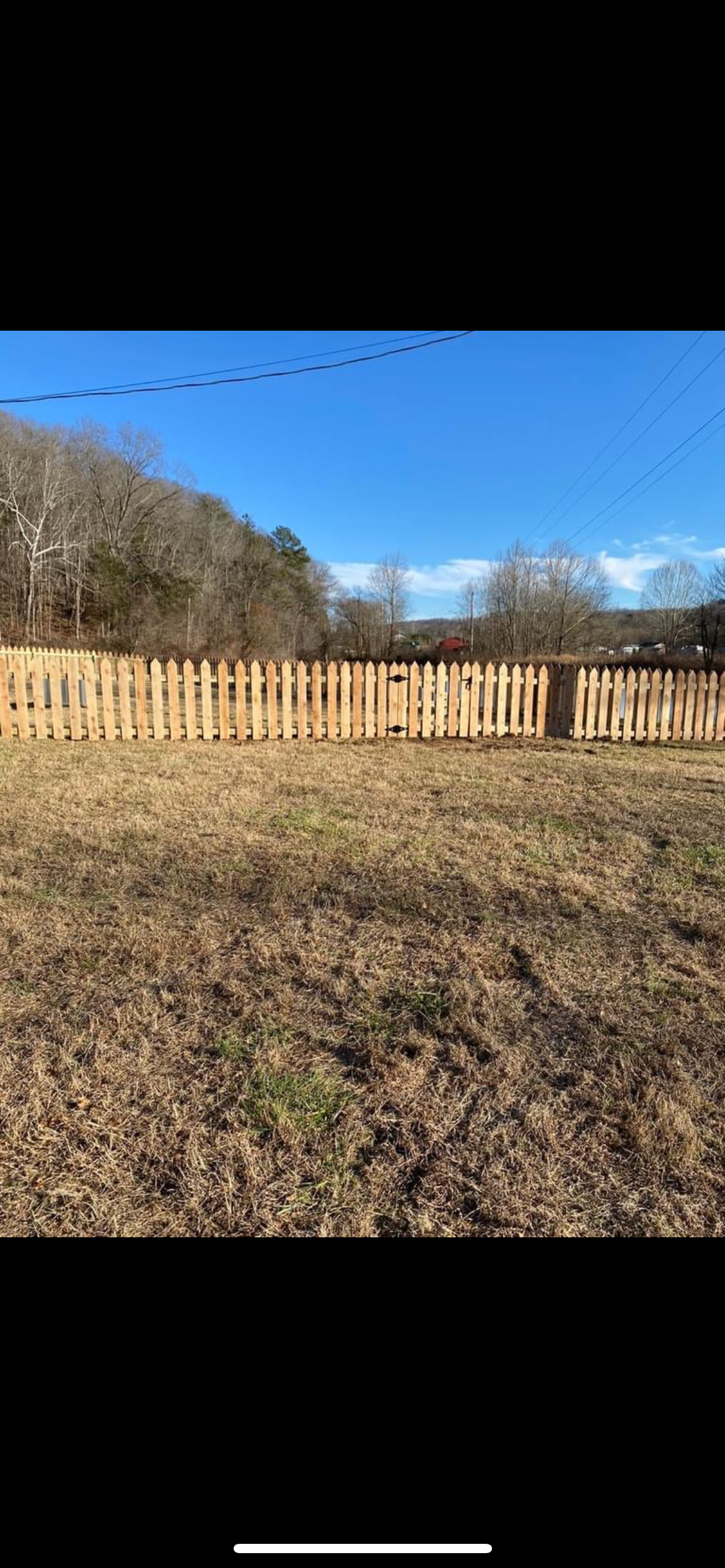 Wooden fence in a field with brown grass and trees, blue sky.