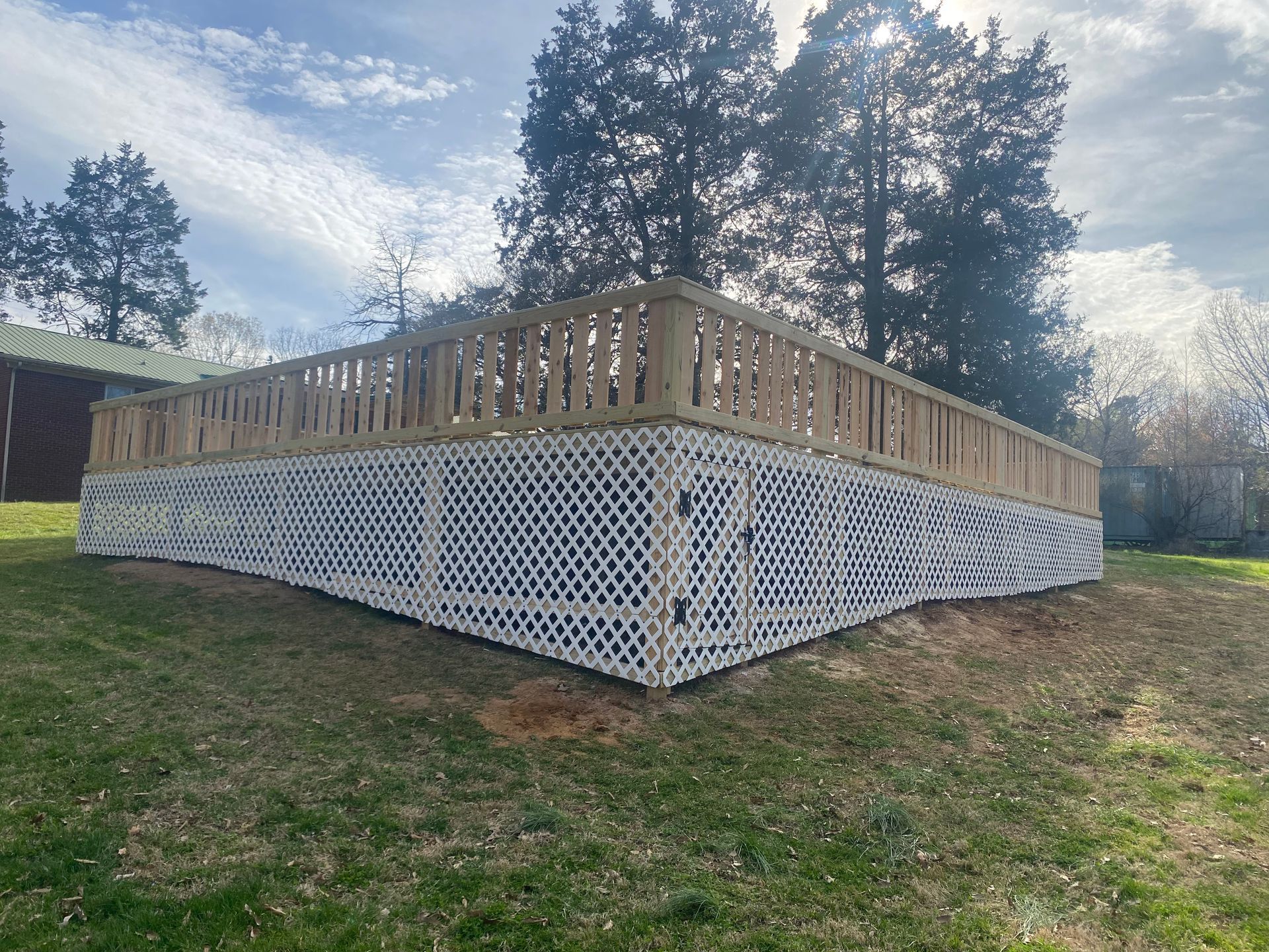 Wooden deck with white lattice skirting and railing, set on a grassy lawn under a cloudy sky.