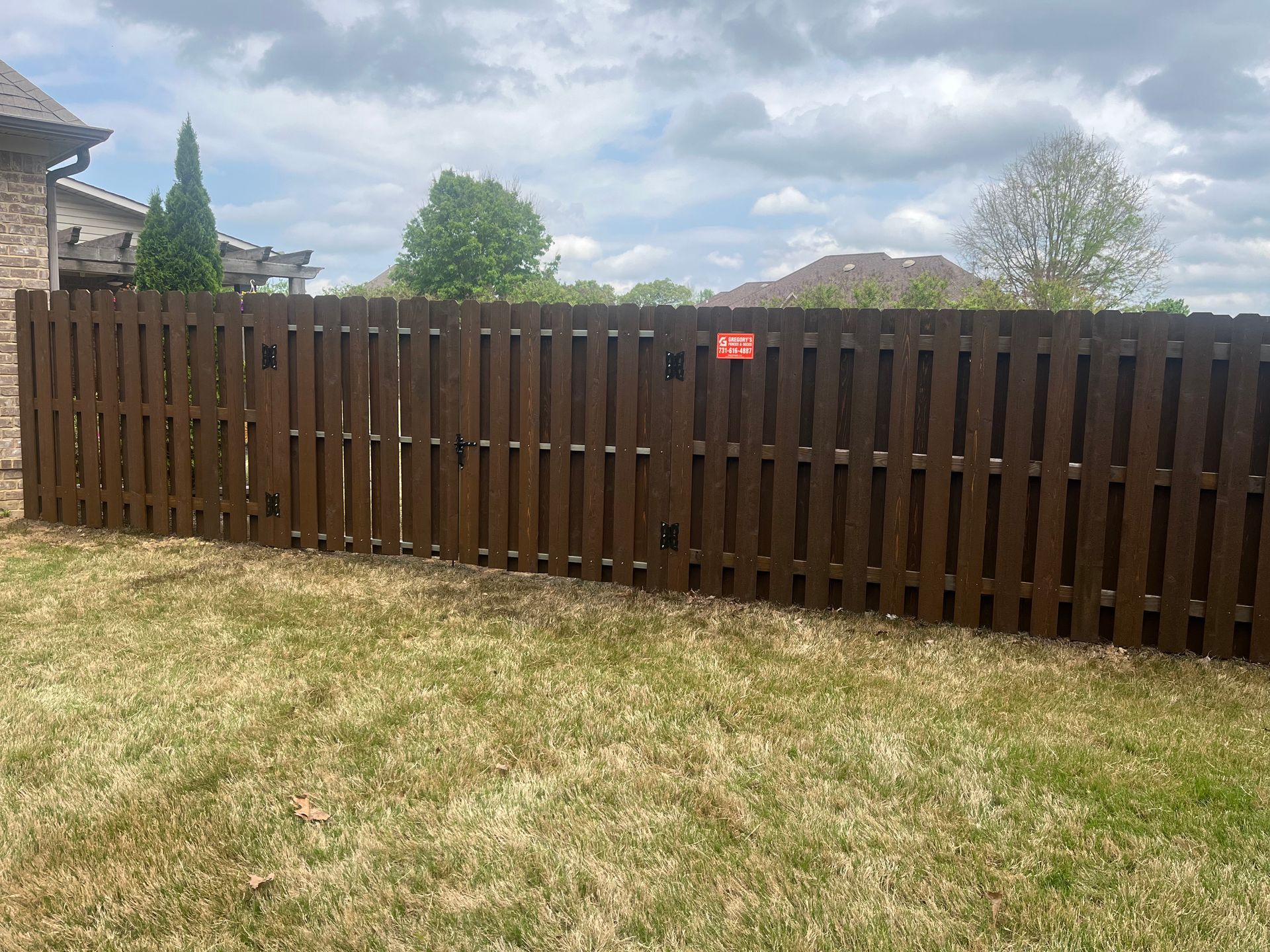 Brown wooden fence in a grassy yard under a cloudy sky.