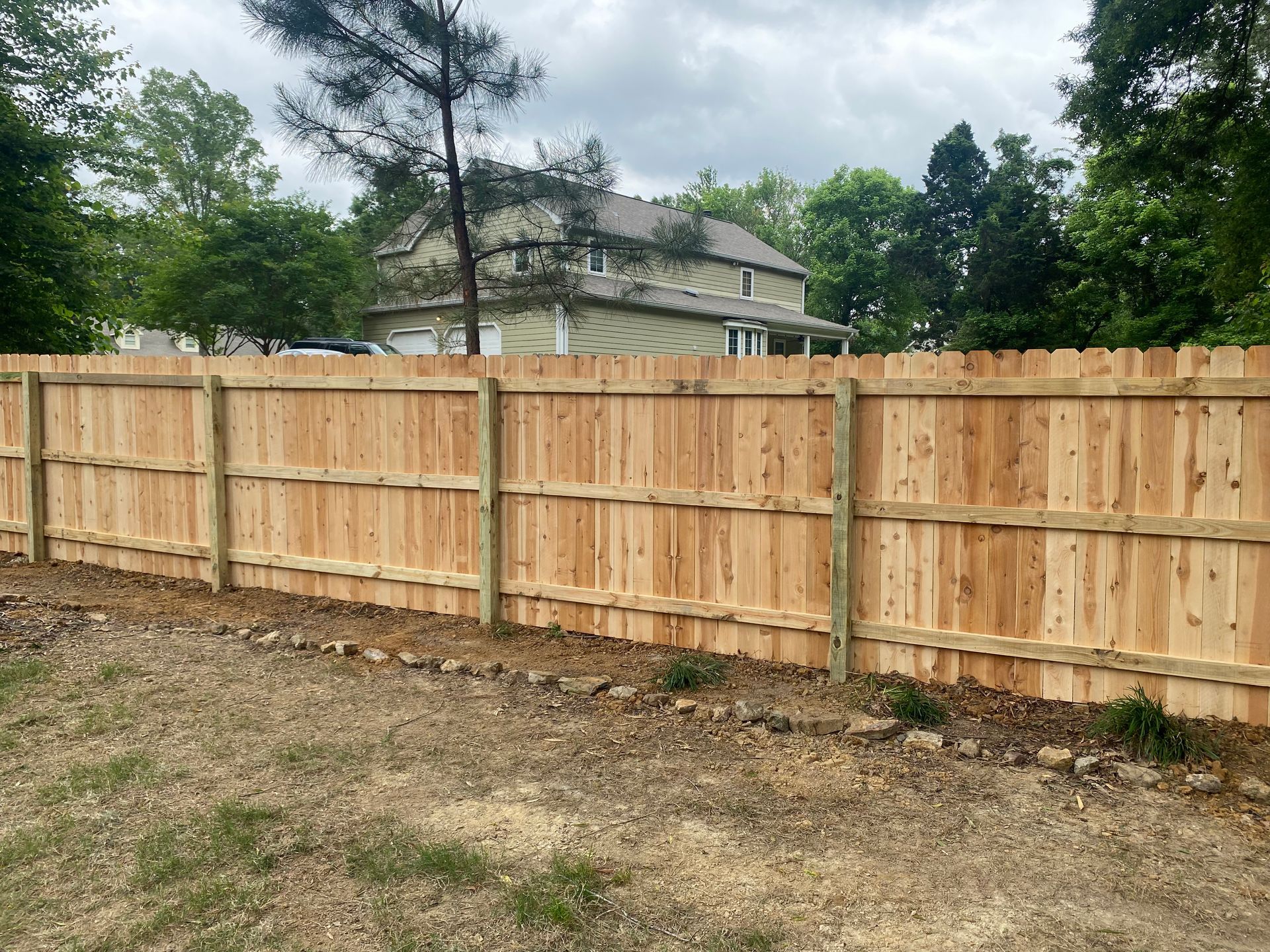 Wooden privacy fence in front of a house, constructed of light brown boards and posts.