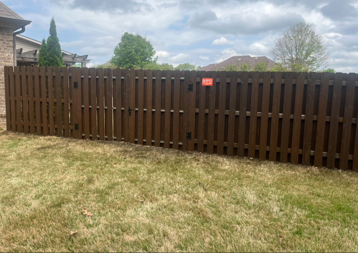 Brown wooden fence in a grassy yard against a cloudy sky.
