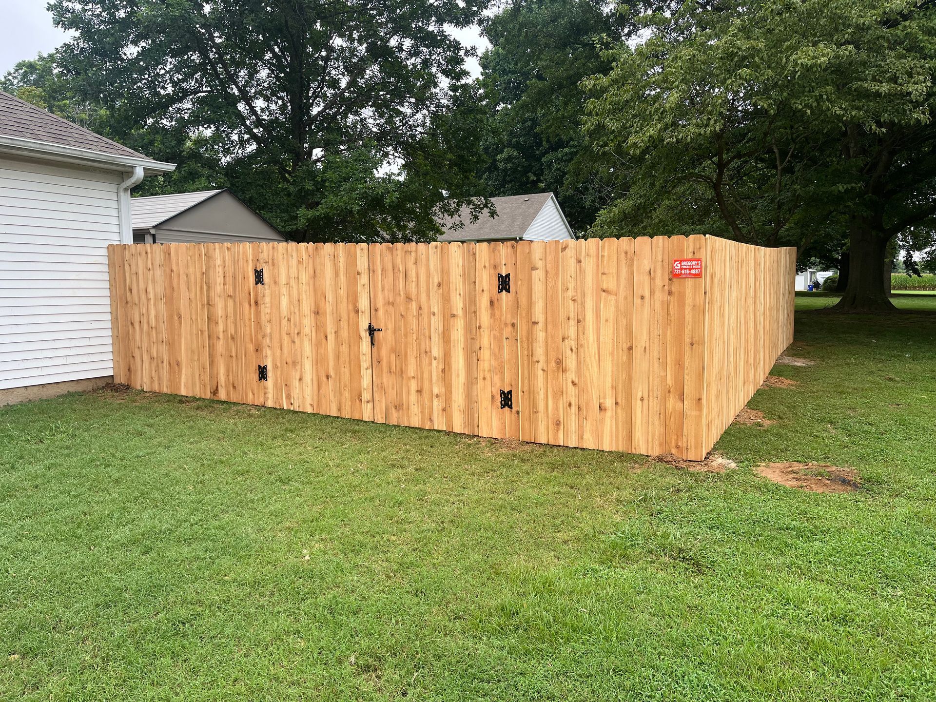 A wooden fence surrounds a grassy backyard.
