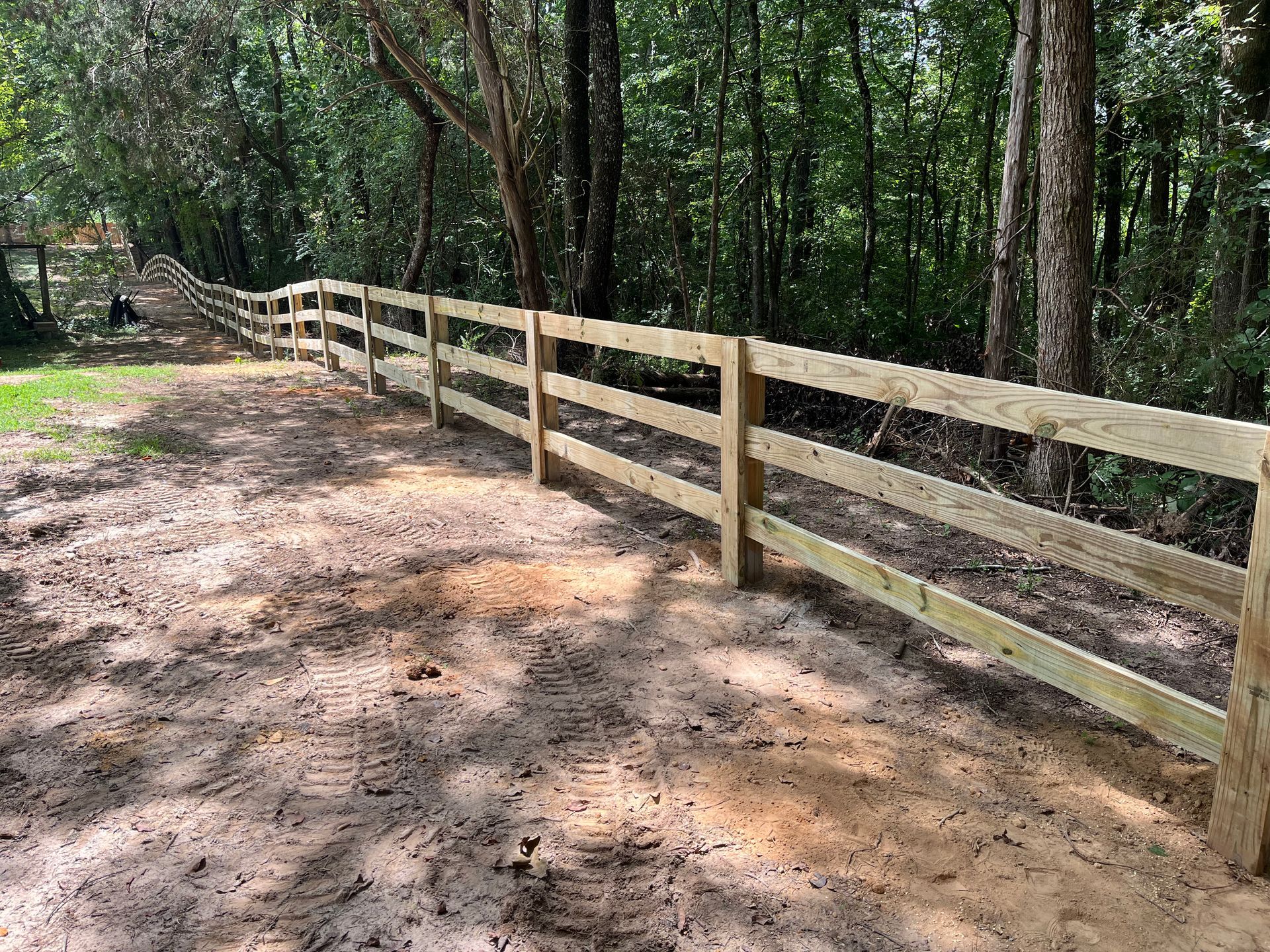 Wooden three-rail fence in a wooded area, likely a property border.