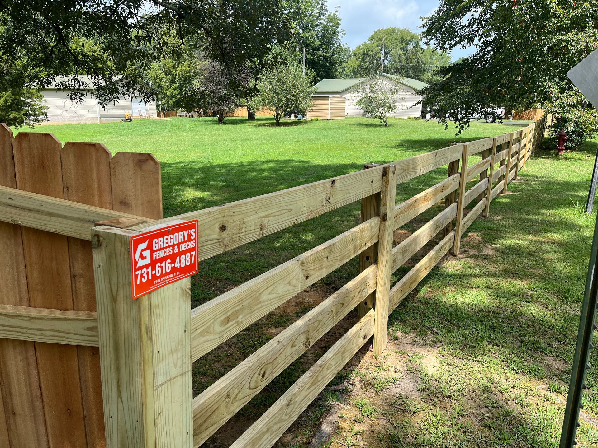 Wooden fence in grassy yard with a house in the background, sunny day.