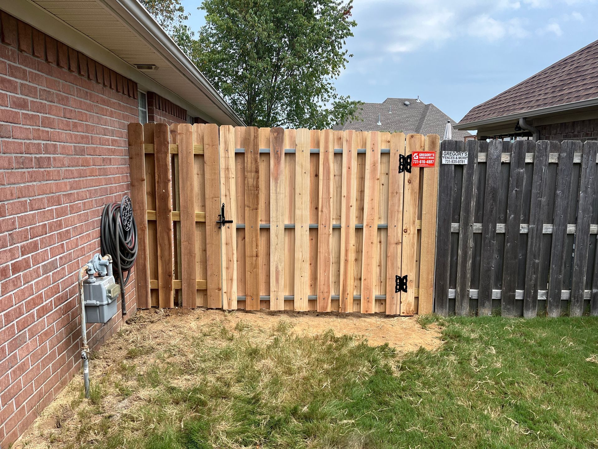 Wooden fence gate between brick house and weathered wooden fence.
