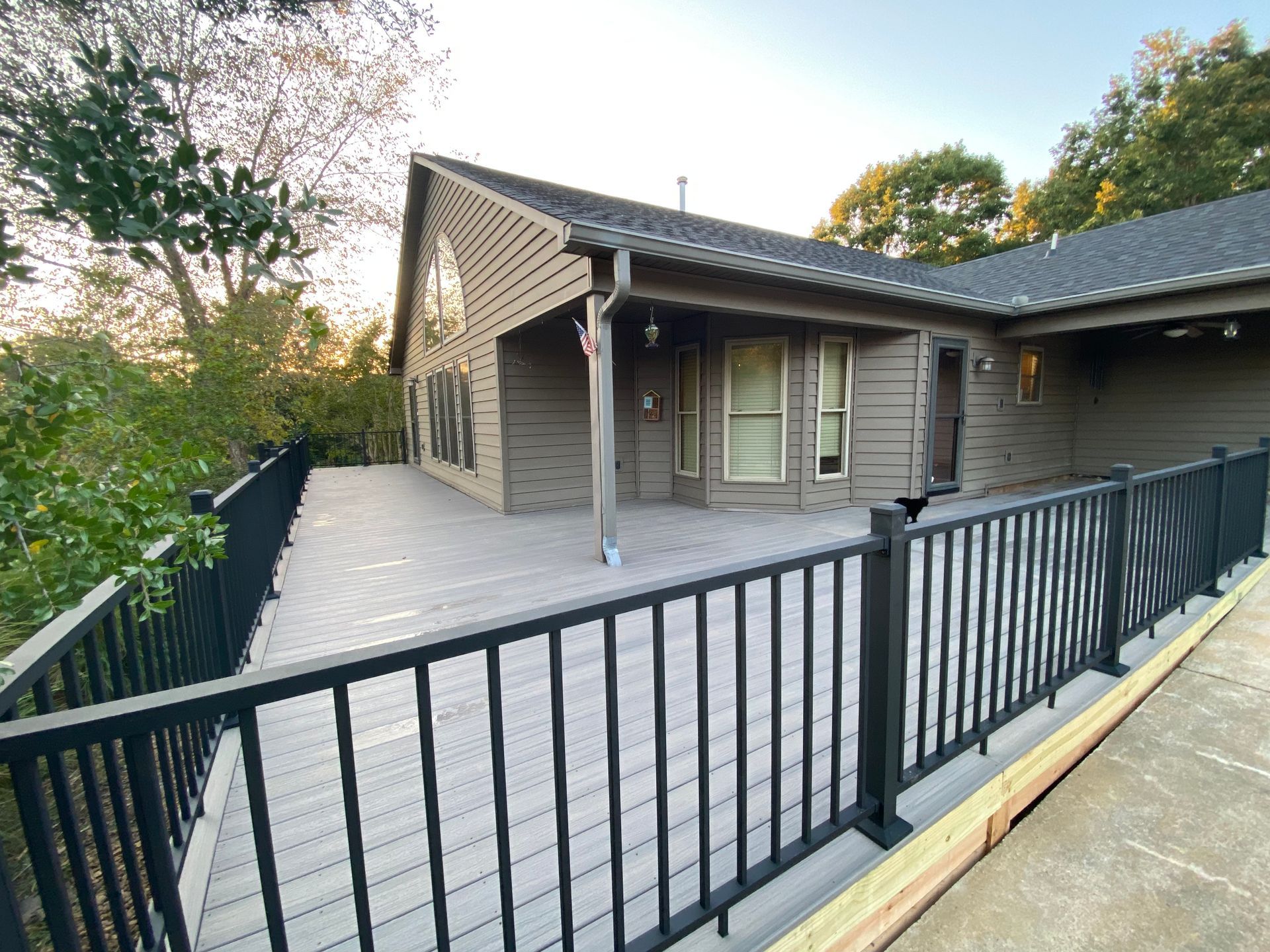 Deck of a house with black railing, gray decking, and brown siding.