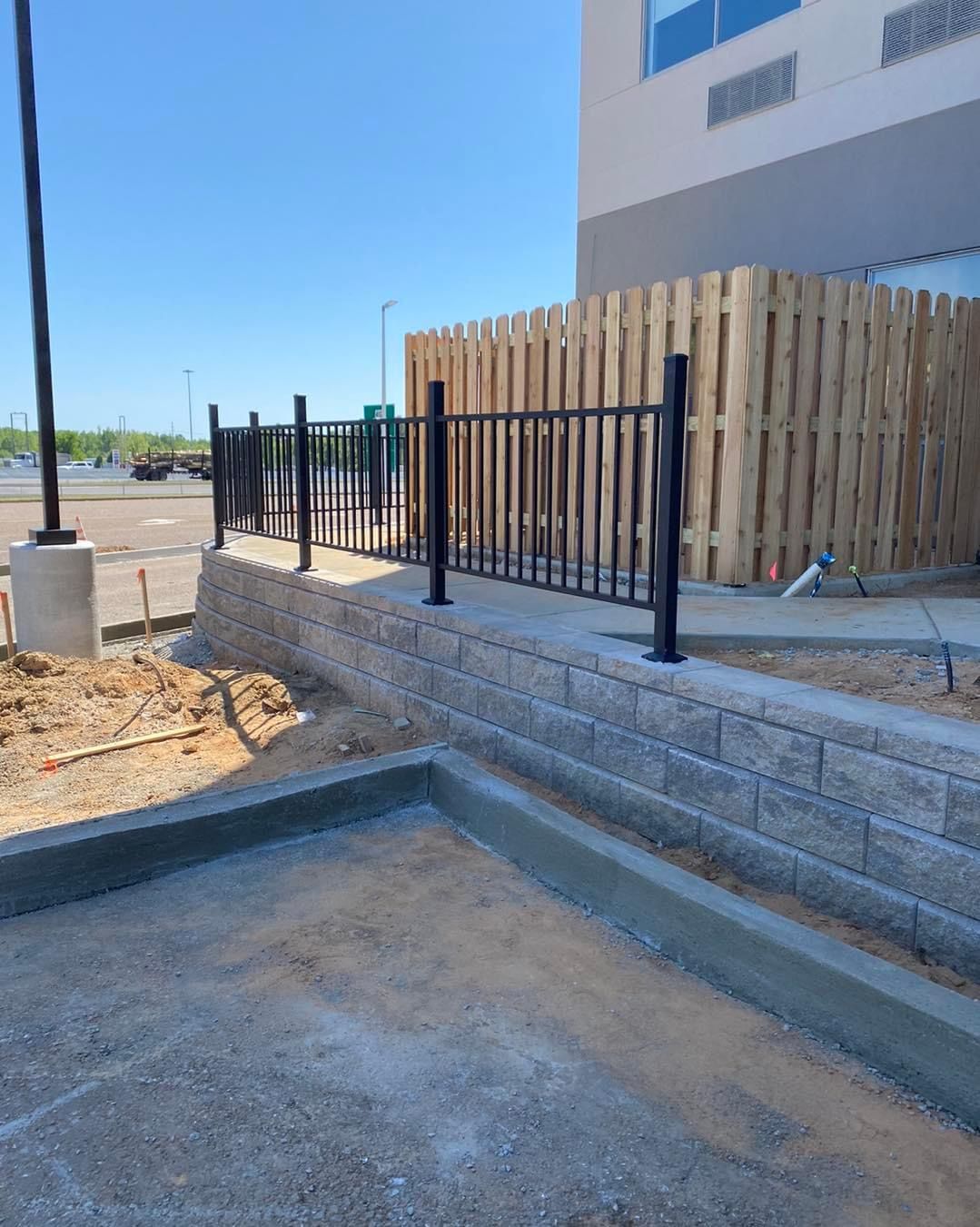 A low retaining wall with a black fence and a wooden privacy fence next to a building.