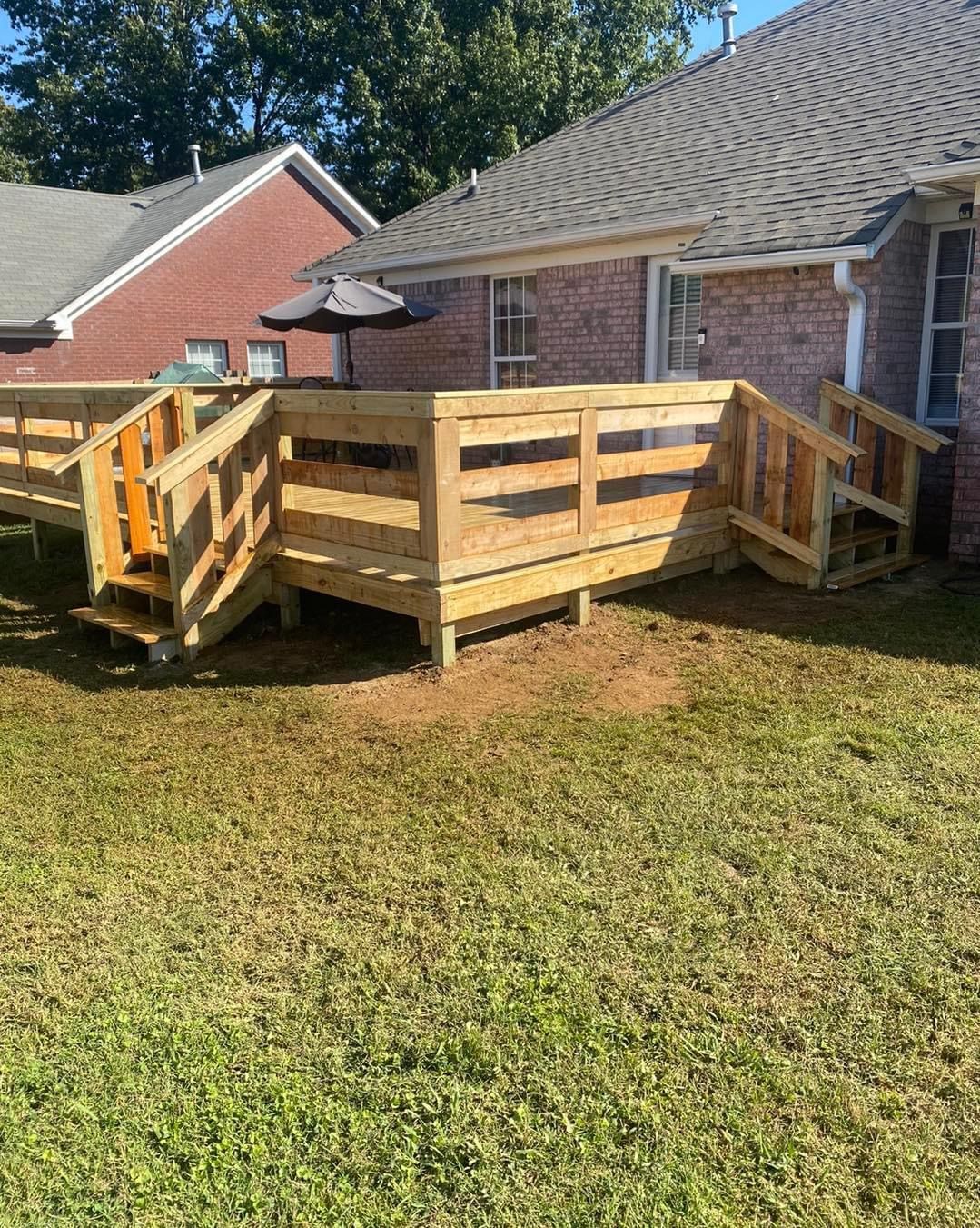 Wooden deck with steps attached to a red brick house, built on a grassy lawn.