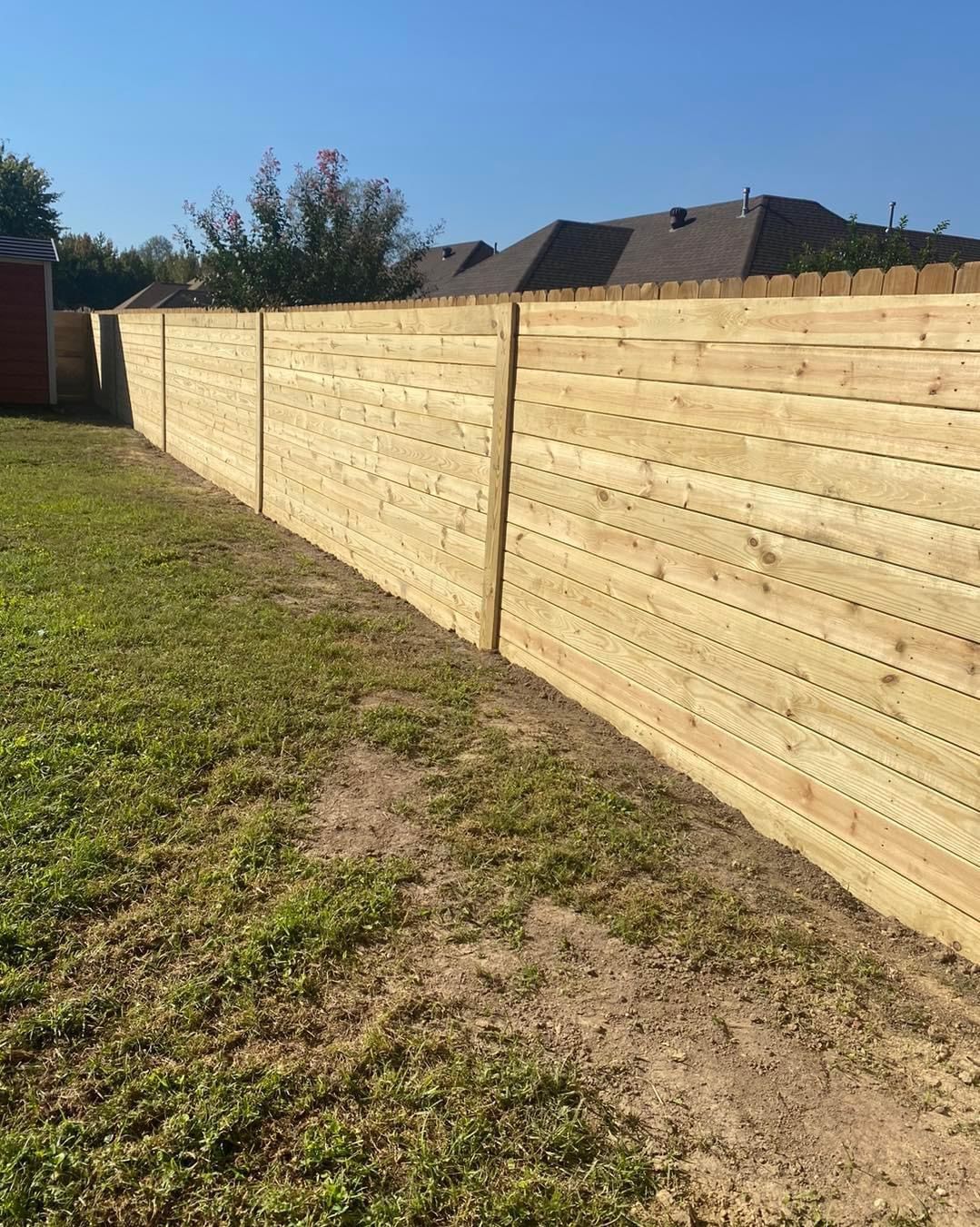 Wooden fence bordering a grassy yard under a clear blue sky.