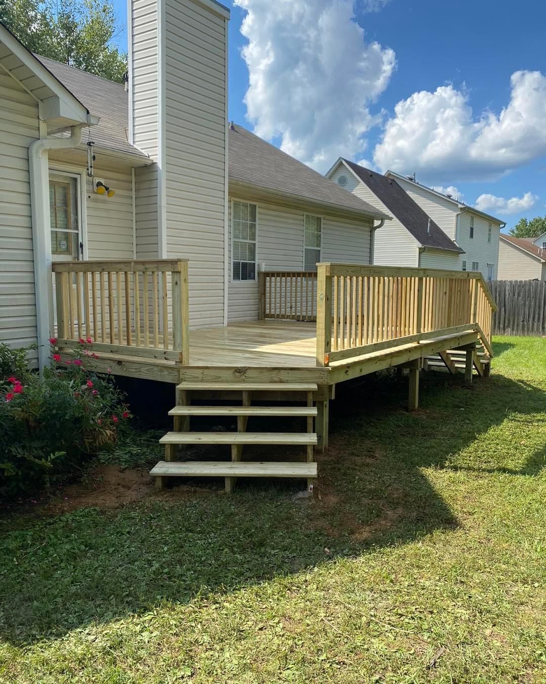 A wooden deck attached to a house, with steps leading to a grassy yard under a blue sky.
