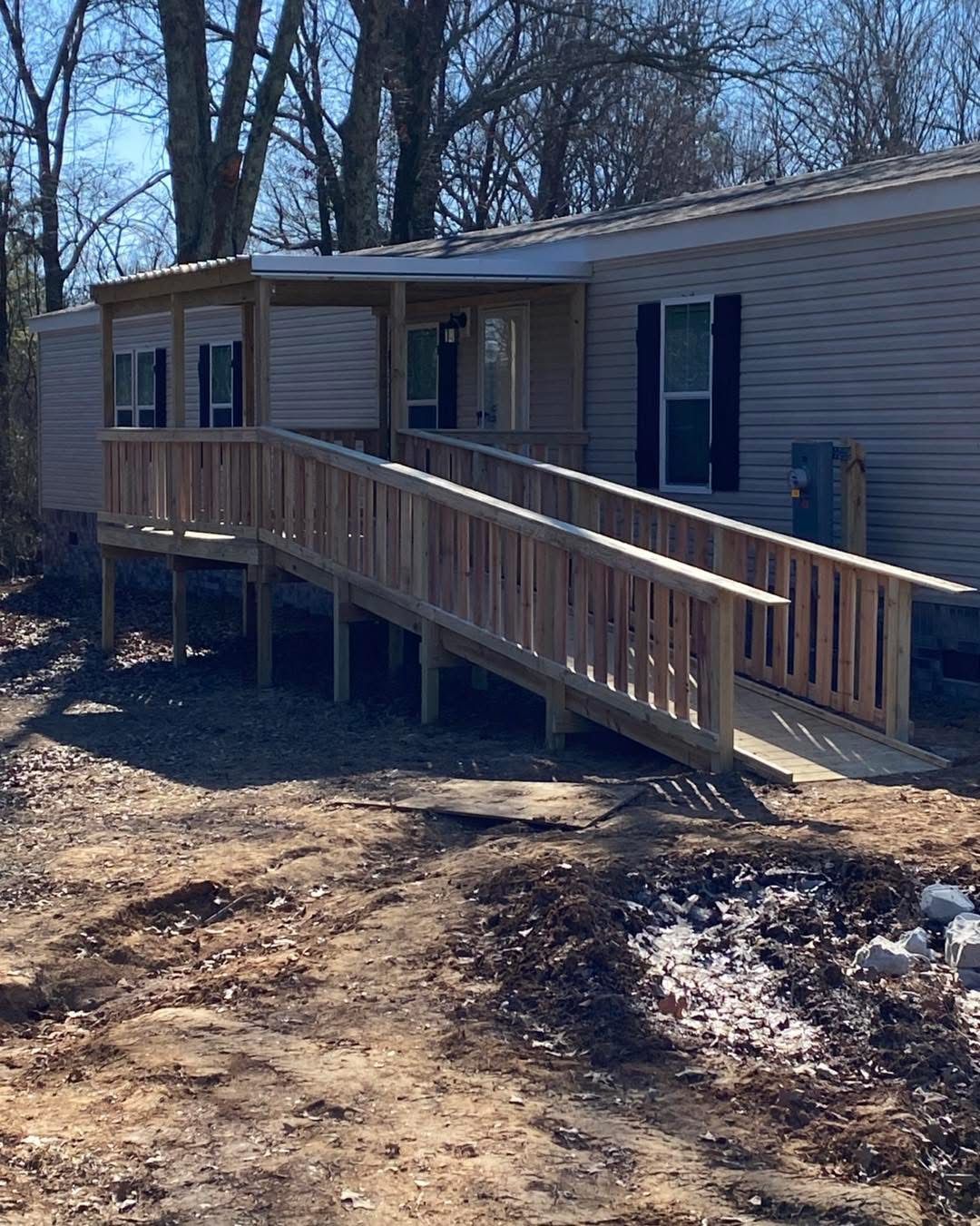 Wooden ramp leading to the front door of a light-colored house with black shutters.