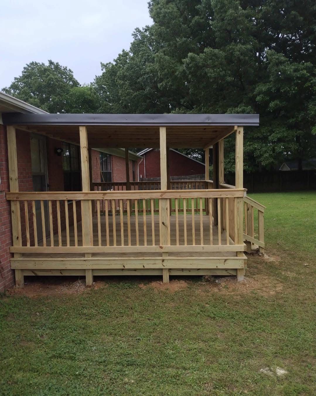 Wooden deck with railing and partial roof attached to a brick building, outdoors.
