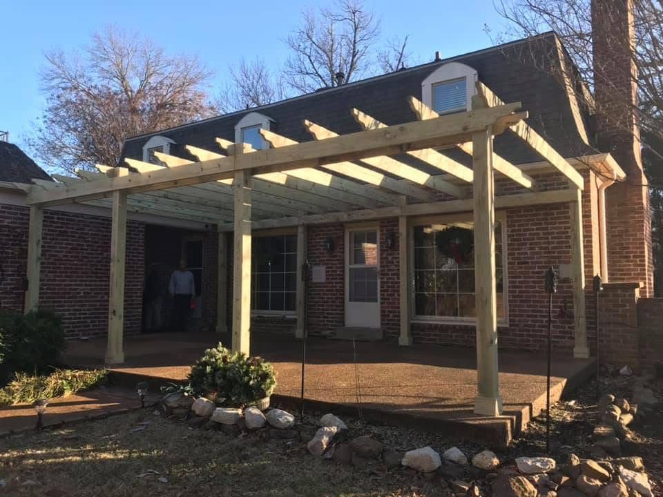 Wooden pergola over a brick patio, attached to a brick house with a dark roof.