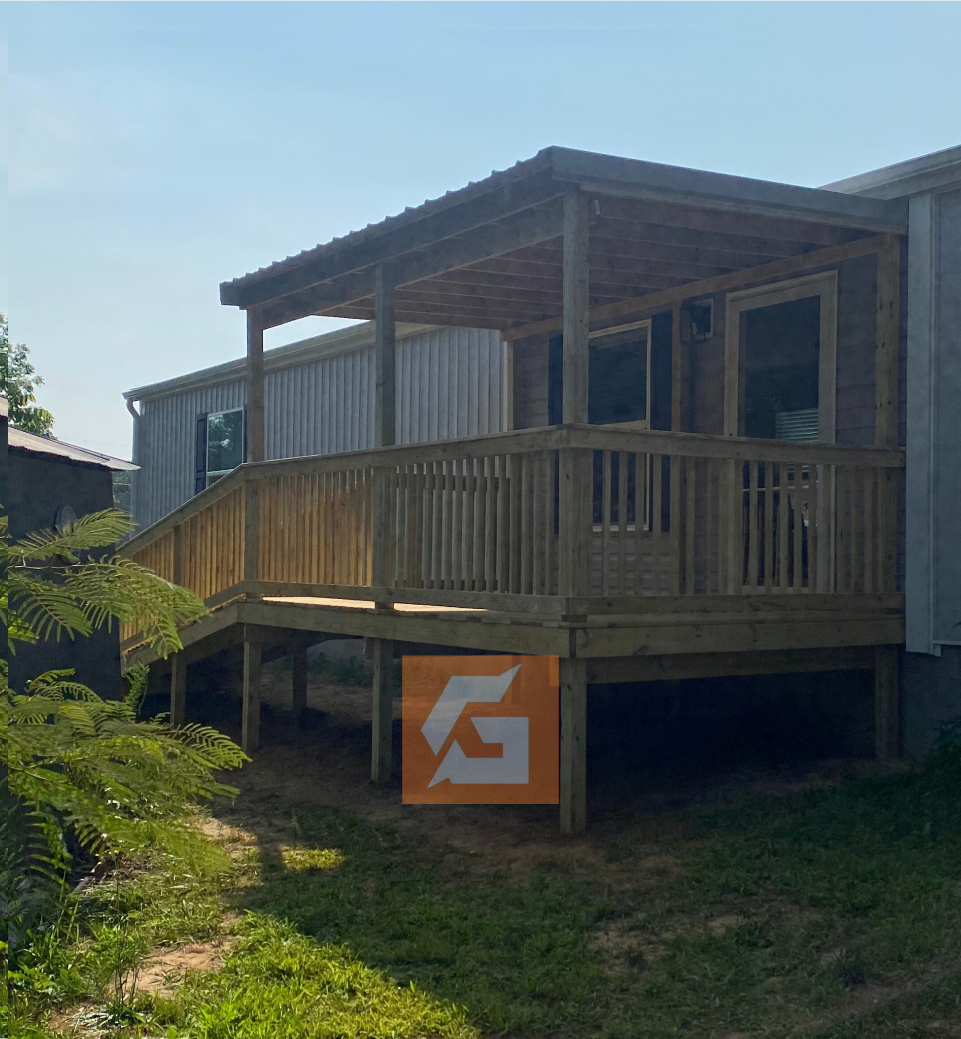 Wooden deck with a ramp and roof, attached to a light-colored building. An orange logo is visible.