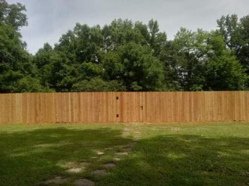 Wooden fence in a grassy yard with trees in the background.