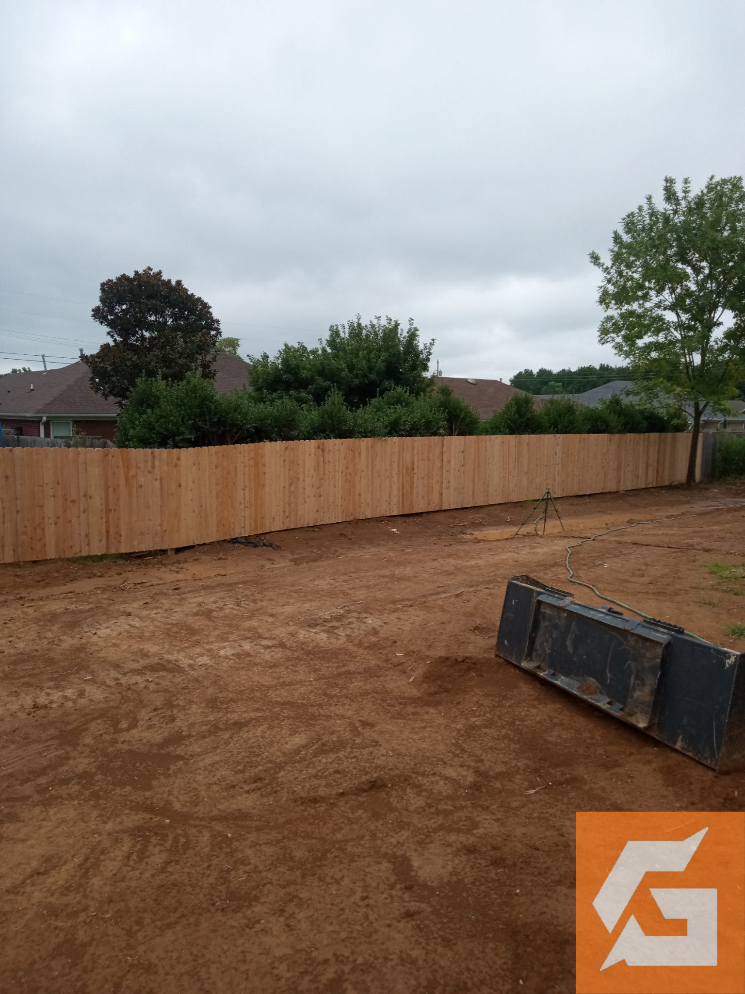 A newly constructed wooden fence encloses a dirt yard under a cloudy sky.