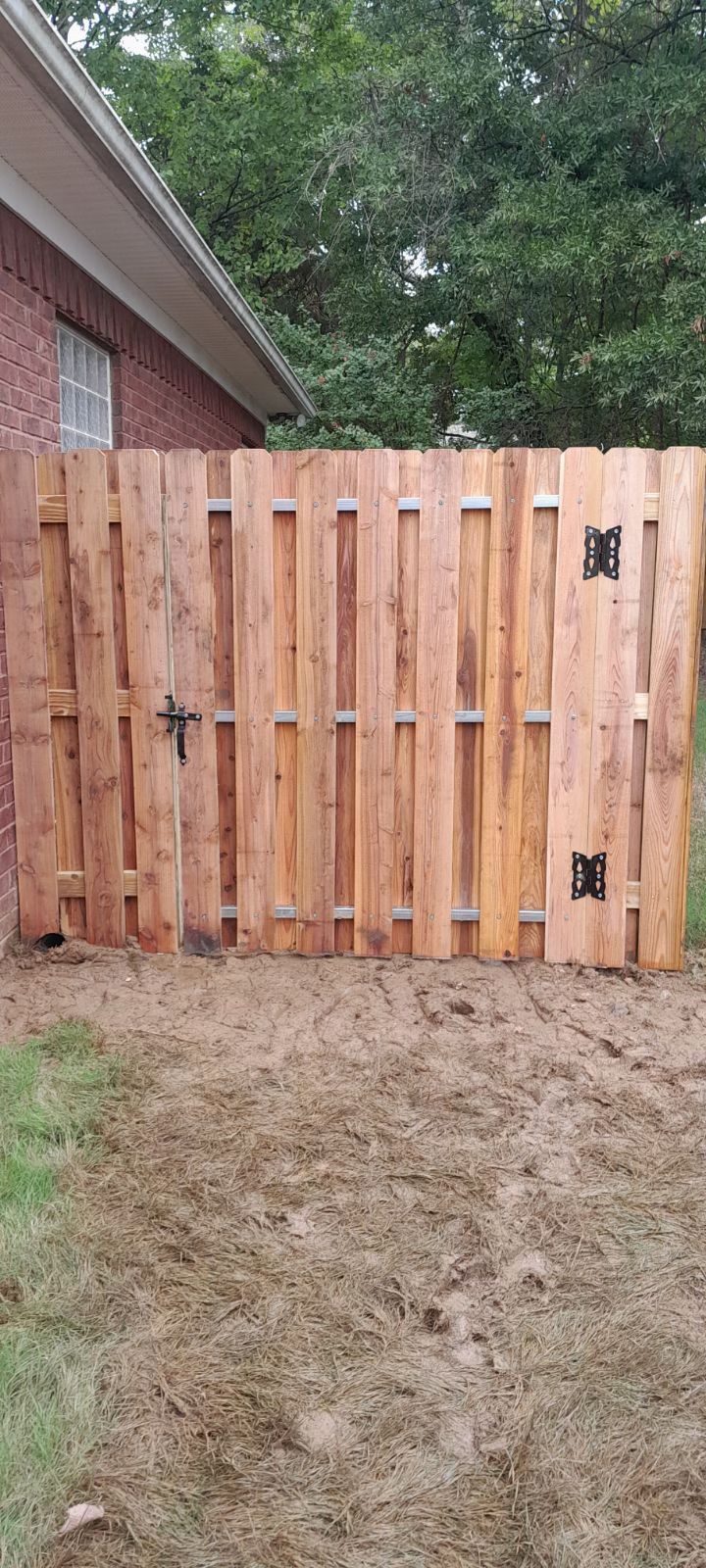 Wooden fence with gate in front of a brick building and some trees.