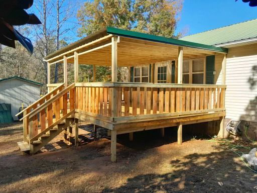 Wooden deck with roof addition, stairs, and railing extending from a house. Green roof and siding.