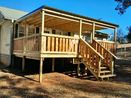 Wooden deck with railing and covered roof attached to a house, stairs lead down.
