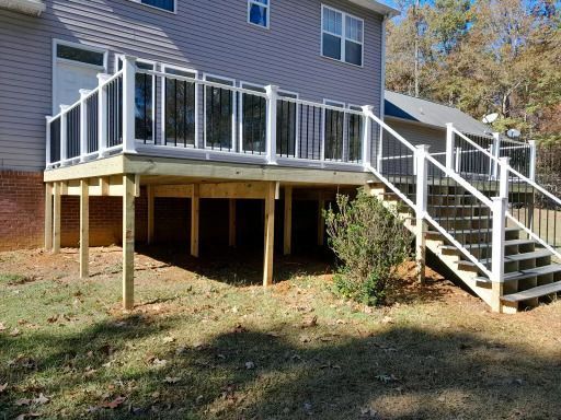 A two-story deck with white railings and stairs, attached to a gray house in a grassy yard.