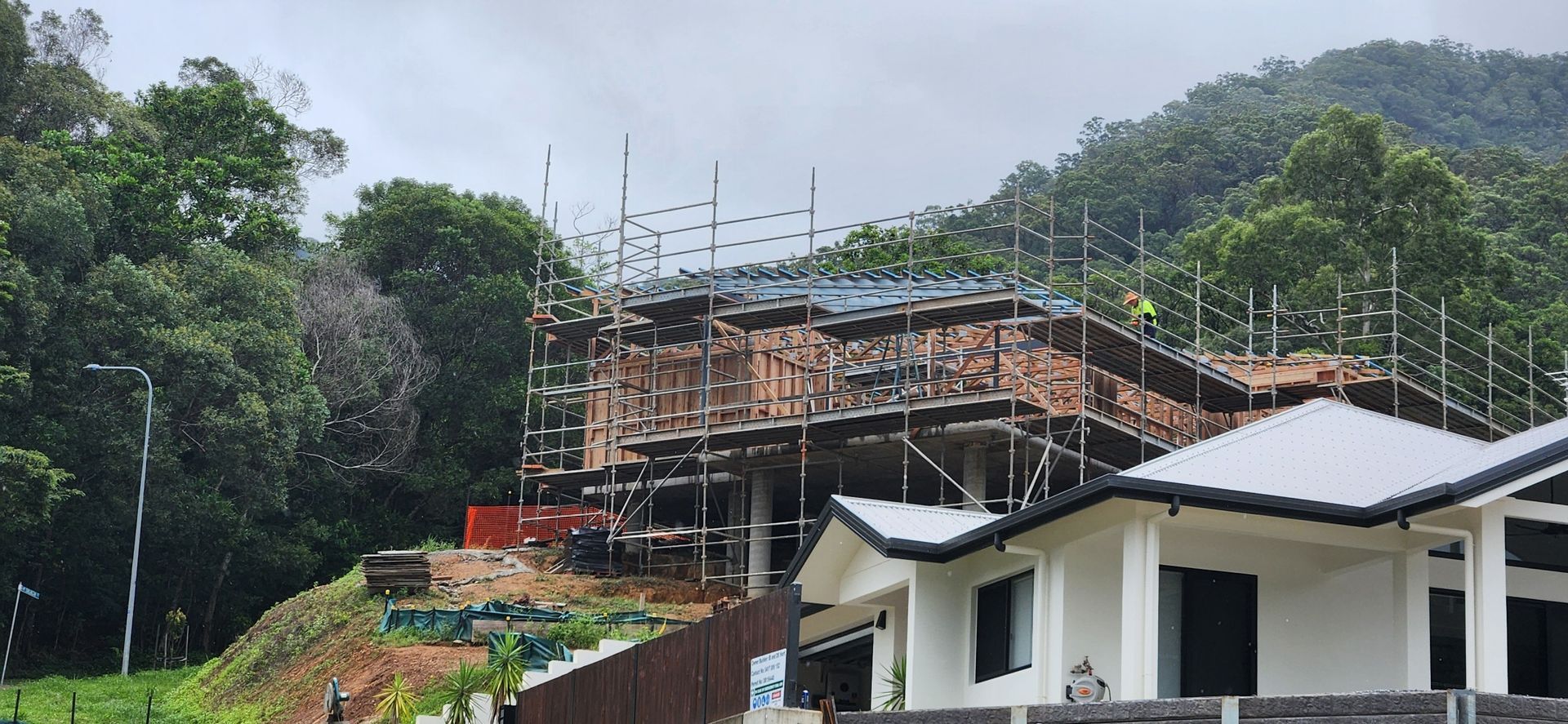 Rural hillside construction site with scaffolding beside a white house and green trees — Underdog Edge Protection in Redlynch, QLD