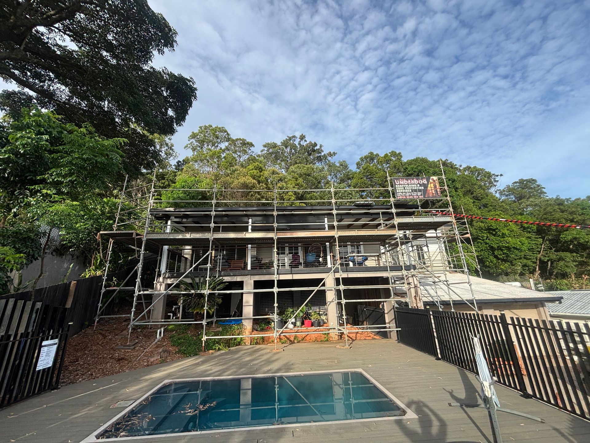 House under construction with a blue-tiled pool in front, surrounded by scaffolding and trees — Underdog Edge Protection in Redlynch, QLD