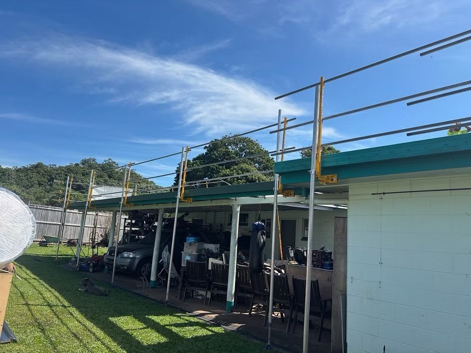 Outdoor carport with parked vehicles under a green roof beside a white building on a sunny day — Underdog Edge Protection in Redlynch, QLD