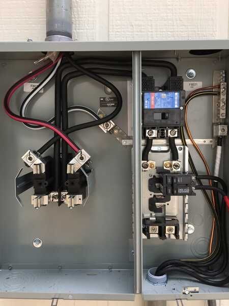 Electrical panel with wires, circuit breakers, and grounding bar inside a metal box.