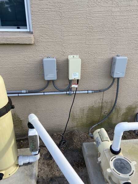 Pool equipment, including pumps and electrical boxes, mounted on a beige wall near the pool.