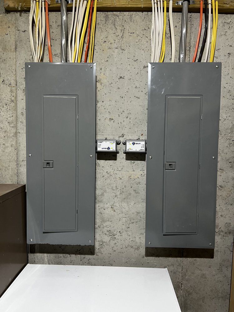 Two gray electrical panels mounted on a concrete wall, with wires and conduits above.