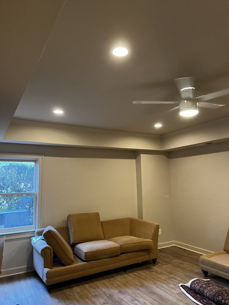Living room with tan couch, ceiling fan, recessed lights, window, and wood-look floor.