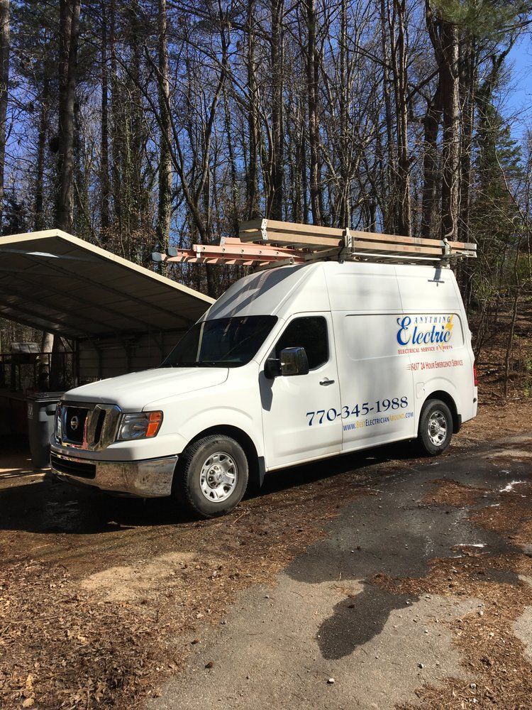 White van with electrical company logo parked outdoors, carrying lumber on a roof rack.