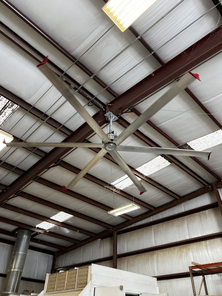 Large, industrial ceiling fan with six silver blades in a warehouse.