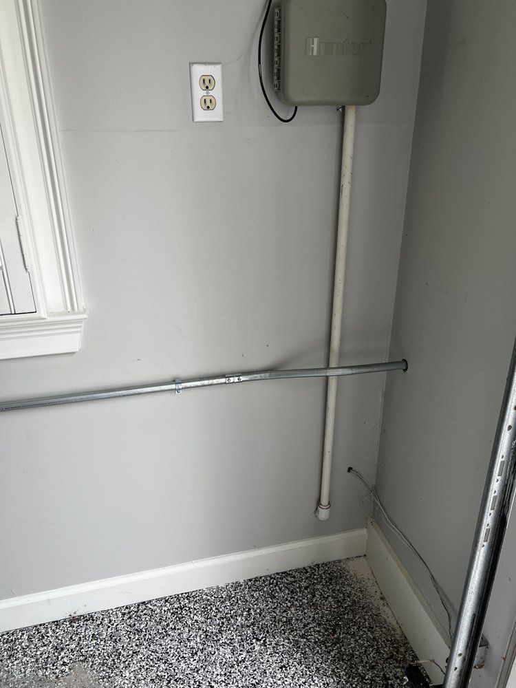 Gray wall with electrical conduits and an outlet.