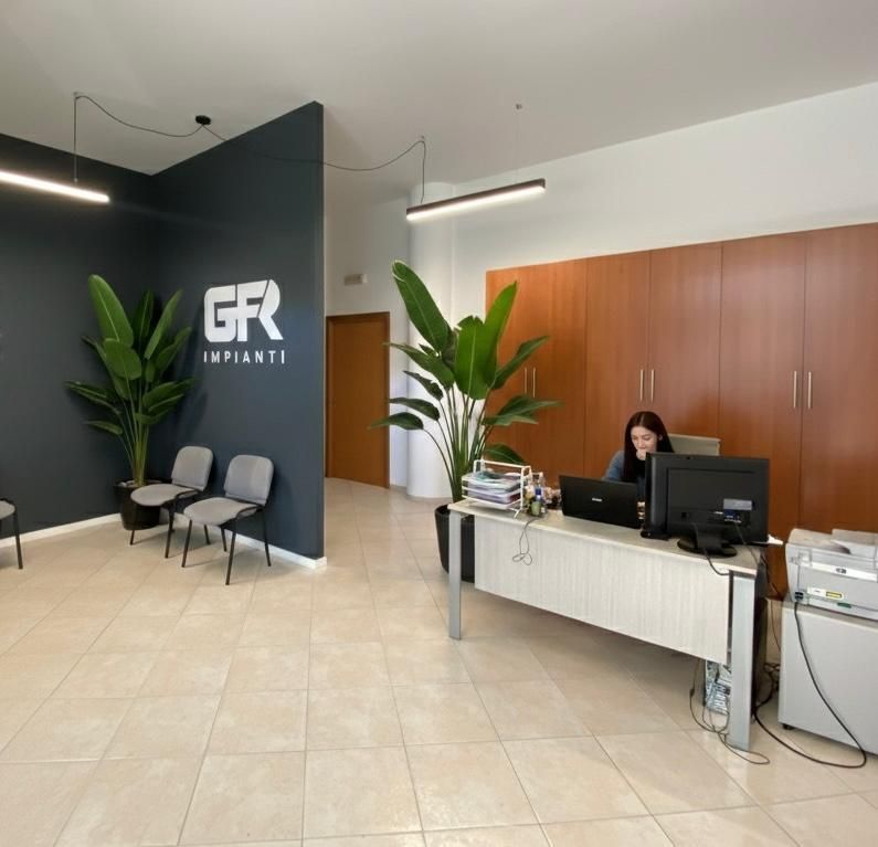 Area reception con scrivania, receptionist, piante e sedie per l'attesa.