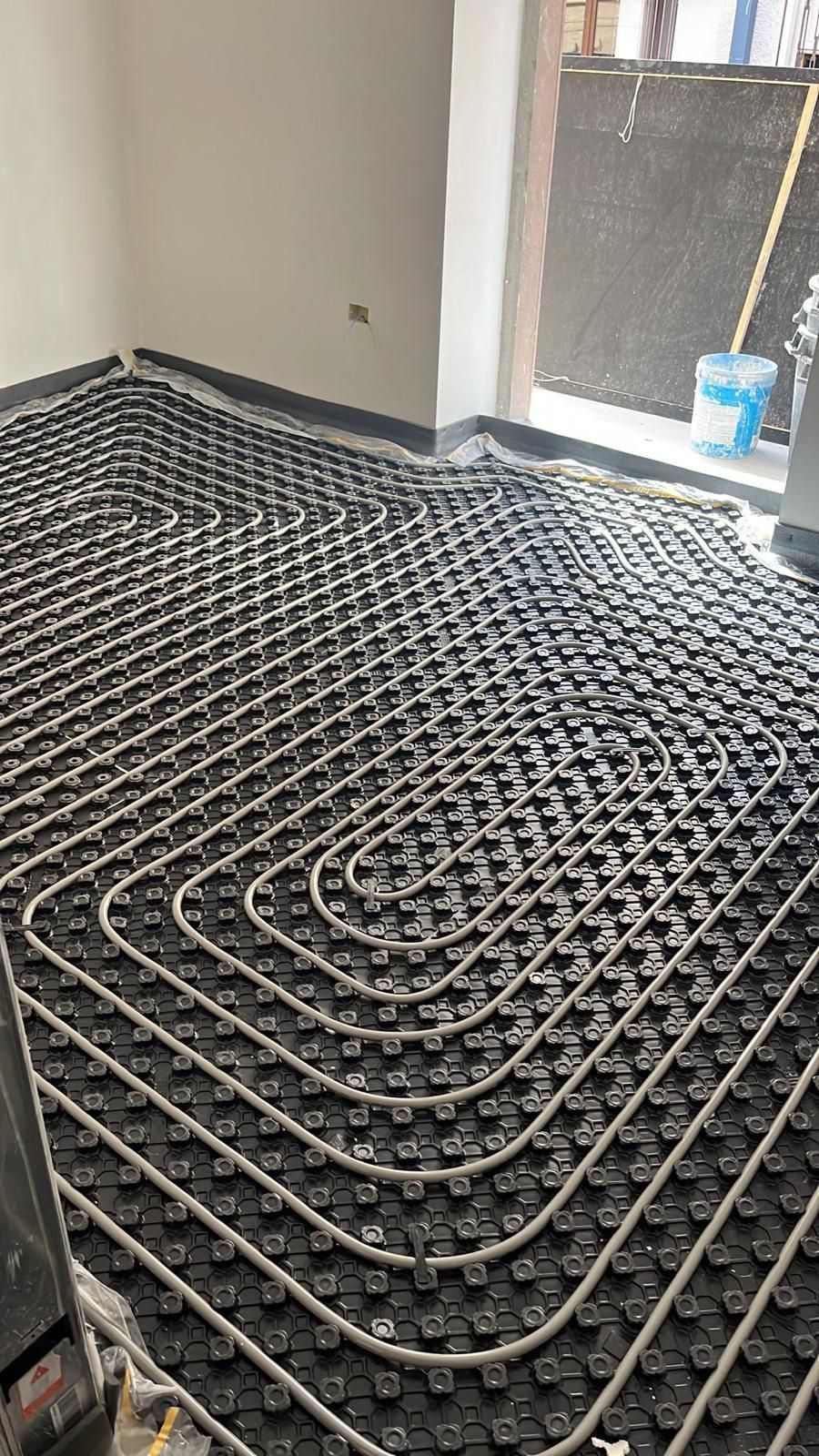 Installazione di un sistema di riscaldamento a pavimento con tubi neri e schema a griglia in una stanza.