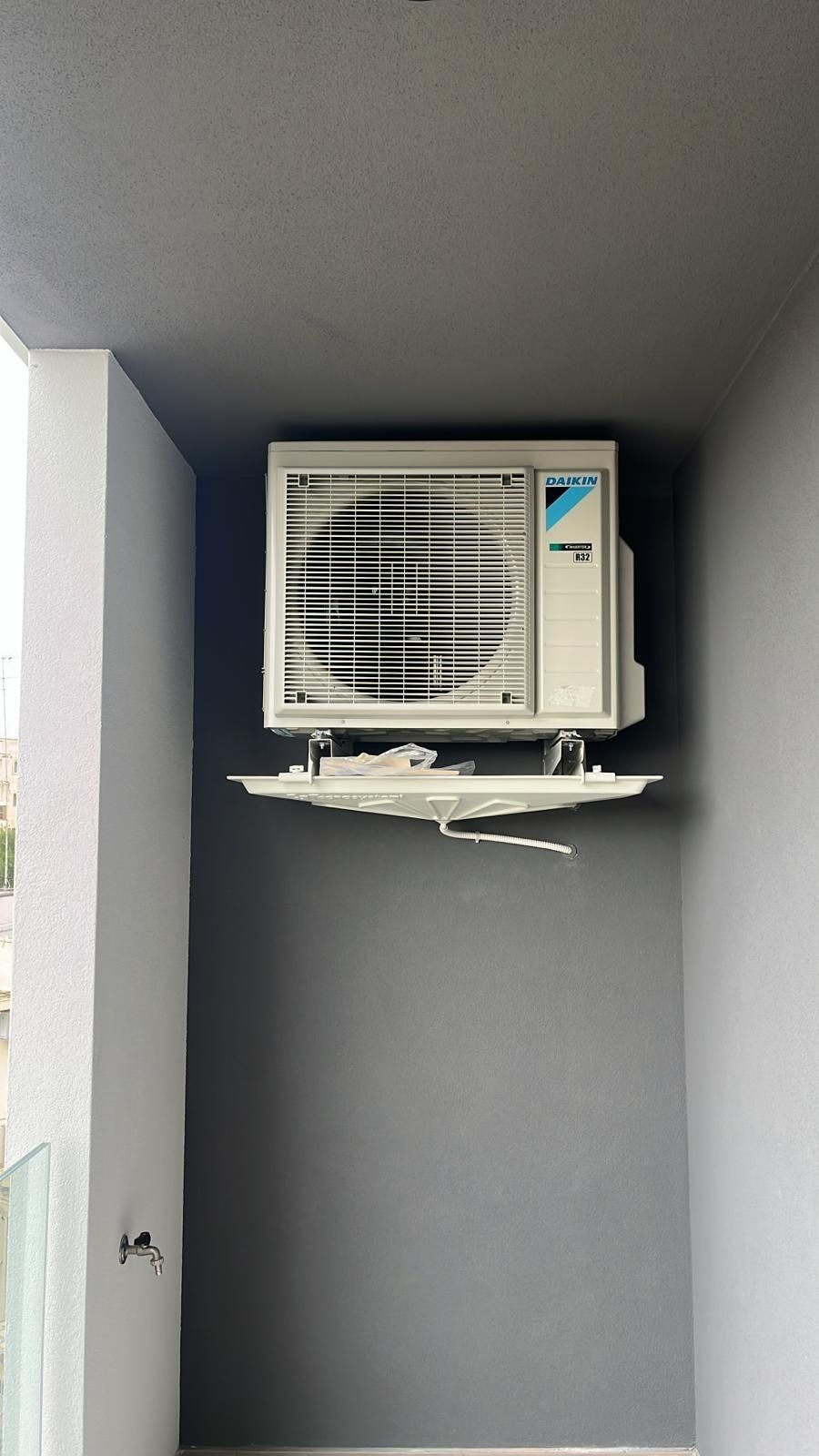 Unità di aria condizionata montata su una parete grigia in uno spazio esterno incassato.