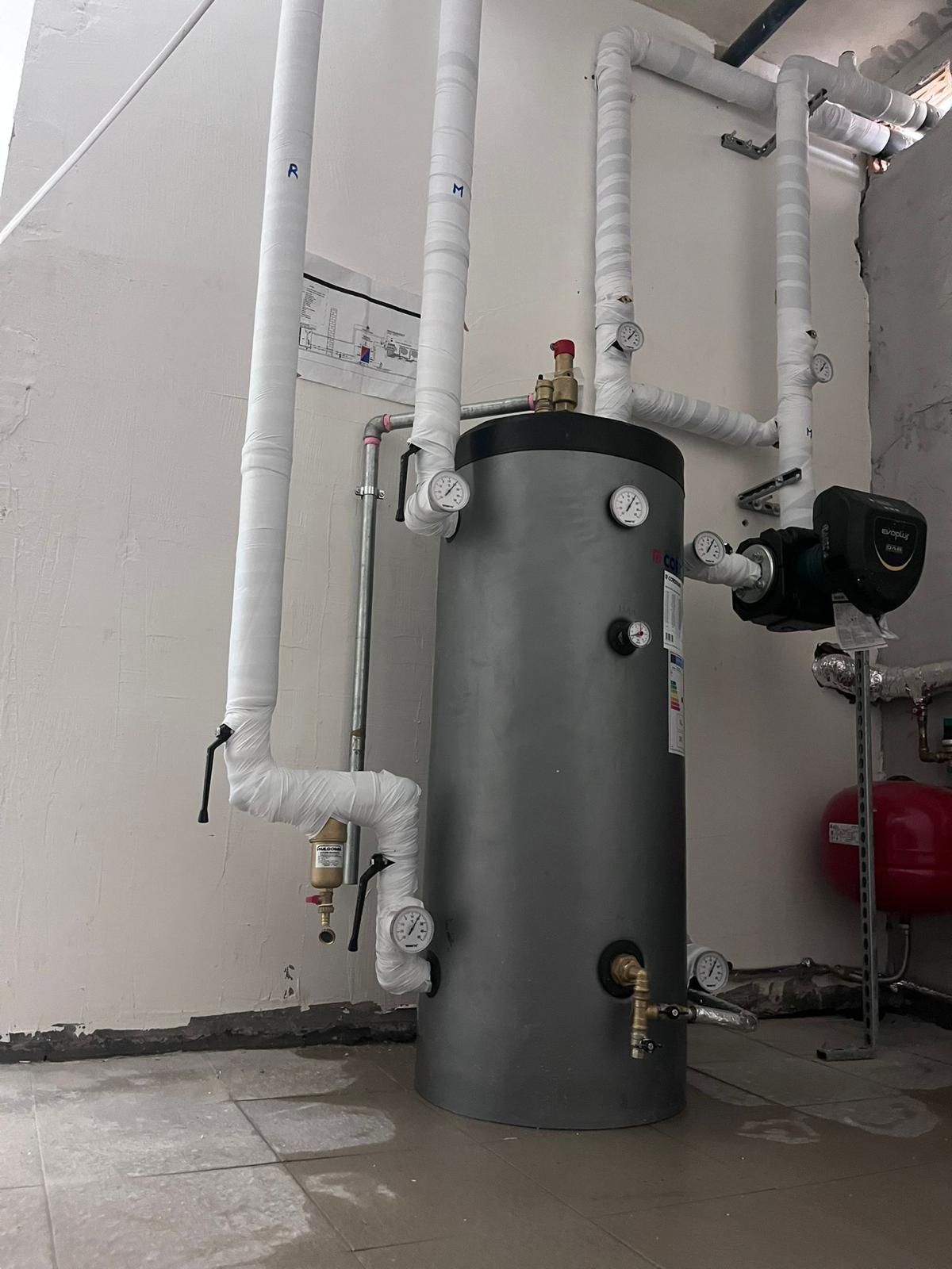 Uno scaldabagno cilindrico con tubi isolati in un ripostiglio.