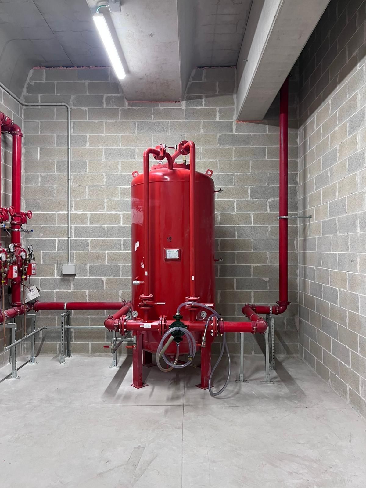 Serbatoio e tubature del sistema antincendio rosso in una stanza di blocchi di cemento.