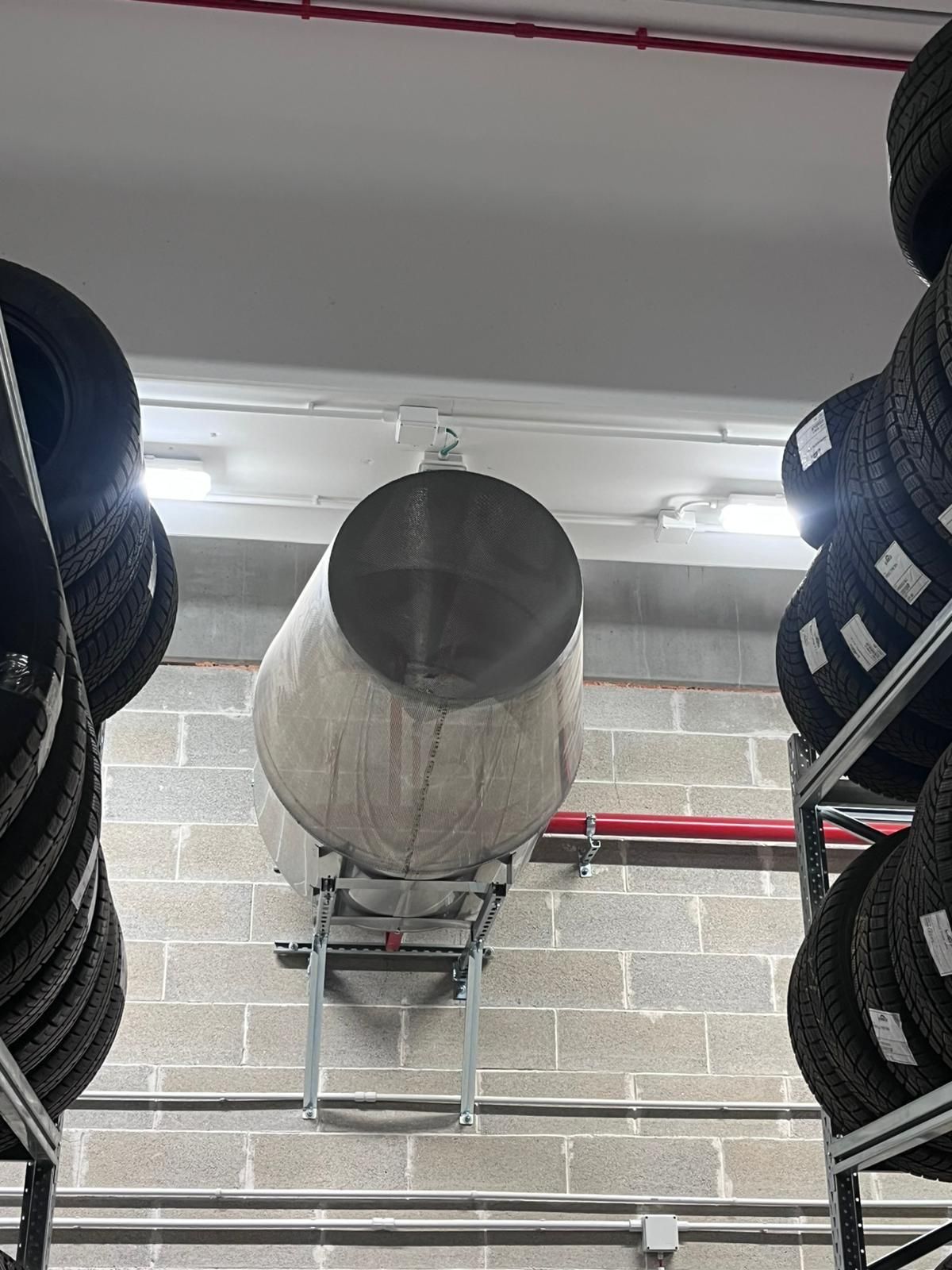 Grande serbatoio cilindrico montato su un muro di mattoni con pneumatici impilati su scaffali su entrambi i lati.