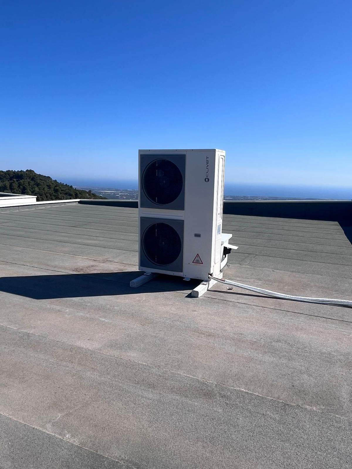 Unità HVAC bianca su un tetto piano, cielo azzurro e oceano sullo sfondo.