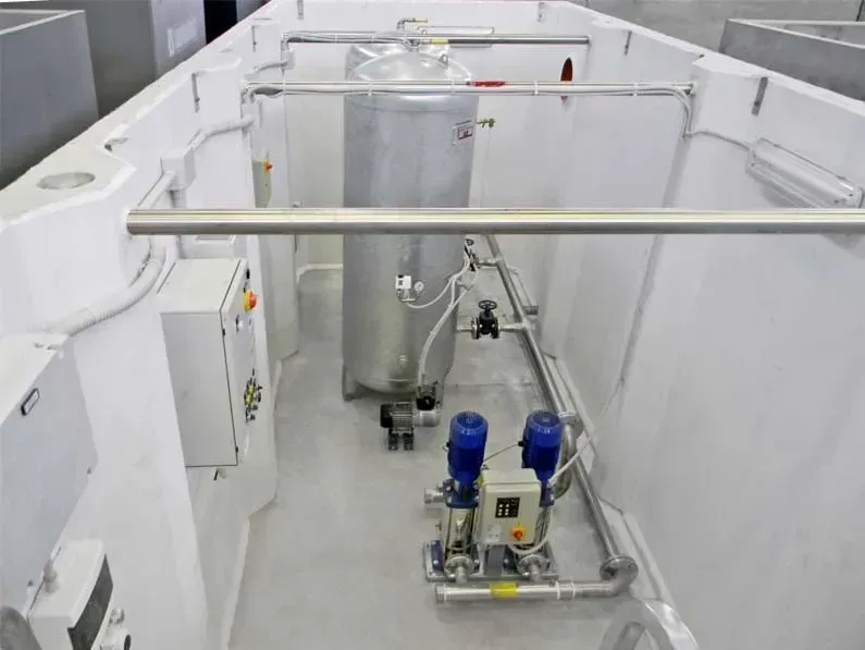 Serbatoio industriale e sistema idraulico all'interno di un recinto con pareti bianche.