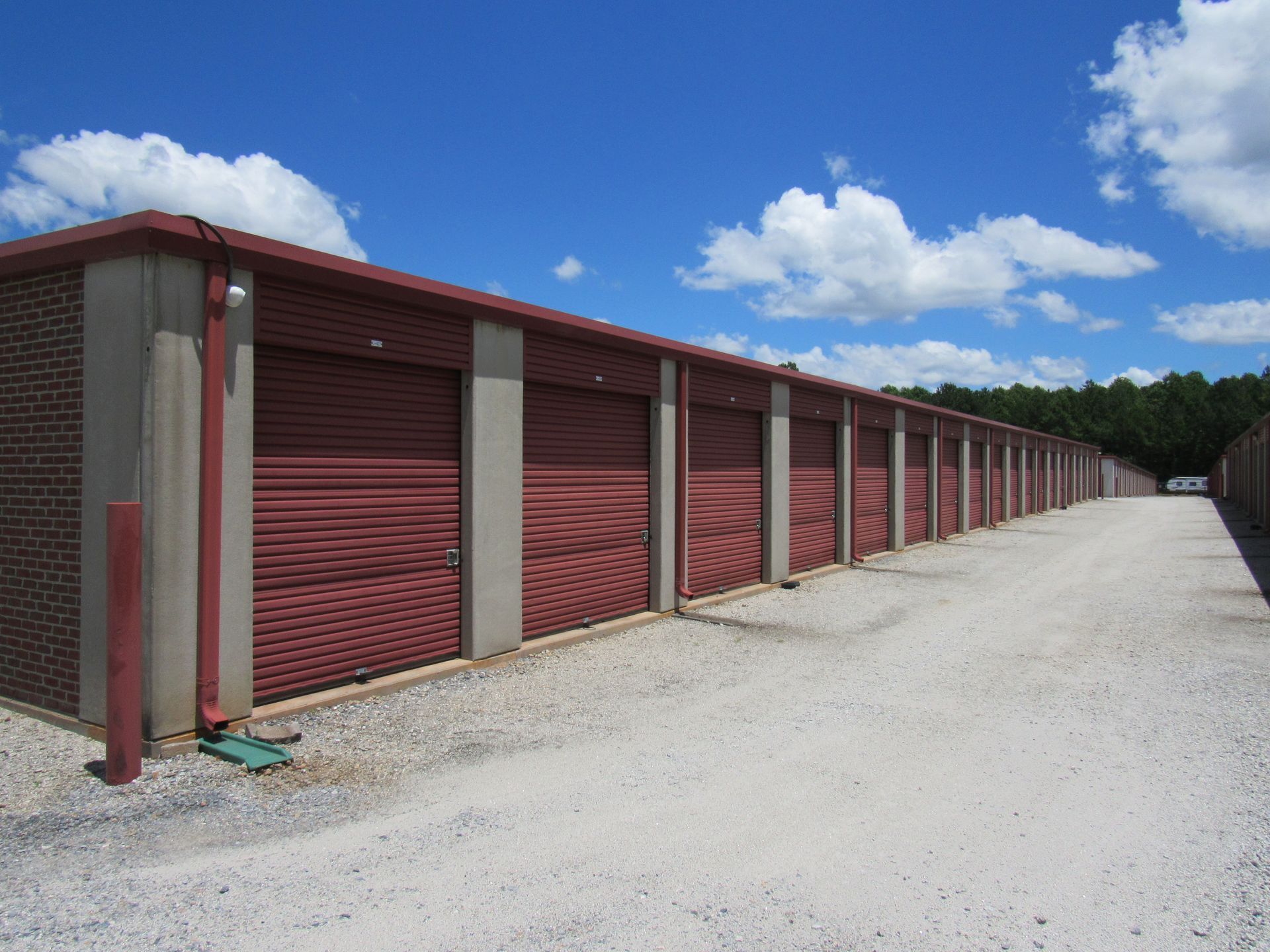 Storage units with red doors and red/gray pillars under a blue sky.