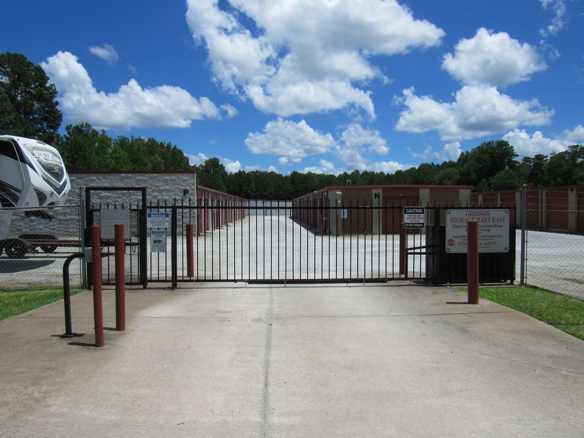 Storage unit facility with gated entrance, tan units, and blue sky with clouds.